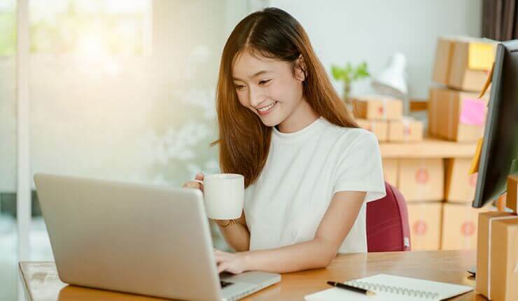 woman smiling at laptop drinking from mug